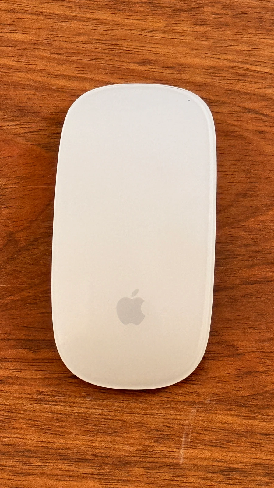 Ahşap yüzey üzerinde beyaz, Apple logolu bilgisayar faresi.