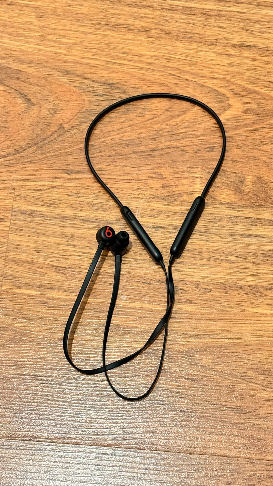 Ahşap zemin üzerinde siyah Beats Flex boyun bantlı kulak içi kulaklık.